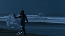 Ариель Домбаль в прозрачном платье бежит по берегу моря